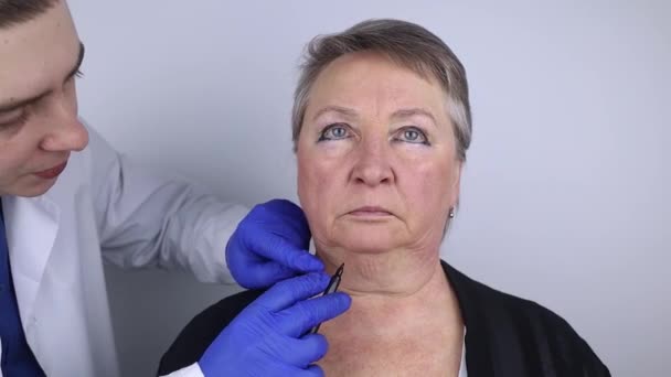 Starsza kobieta w recepcji chirurga plastycznego. Konsultacje w sprawie usuwania zmarszczek wieku na twarzy. Lekarz pokazuje, jakie procedury wykona. Zmarszczki naśladowcze - Materiał filmowy, wideo