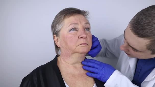 Пожилая женщина на приеме у пластического хирурга. Консультация по устранению возрастных морщин на лице. Врач показывает, какие процедуры он будет делать. Мимические морщины - Кадры, видео