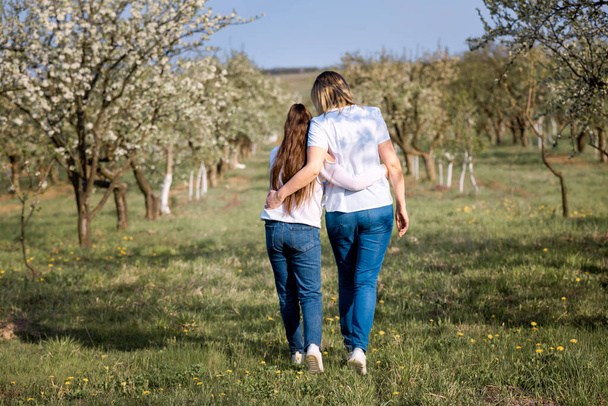 Mom and girl going across the field. Spring vacation, beautiful garden. - Valokuva, kuva