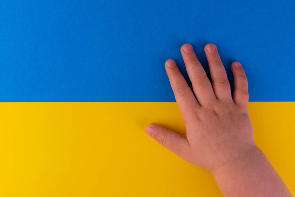 Die Hand eines kleinen Kindes auf dem Hintergrund der Flagge der Ukraine. Konzept gegen den Krieg in der Ukraine. Kopierraum. - Foto, Bild