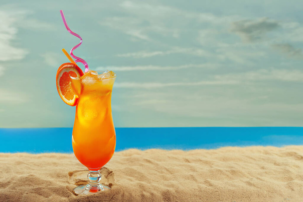 Orange cocktail on the beach. Alcoholic drink with ice, orange on the sand close up. Sunset, sea and sky in the background. Copy space and free space for text near the glass. - Фото, зображення