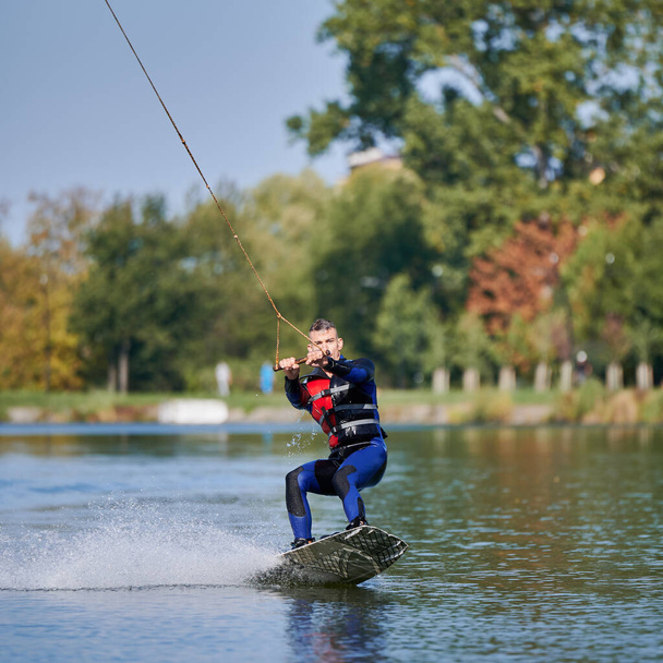 Νεαρός σέρφερ διασκεδάζει wakeboarding στο καλωδιακό πάρκο. - Φωτογραφία, εικόνα