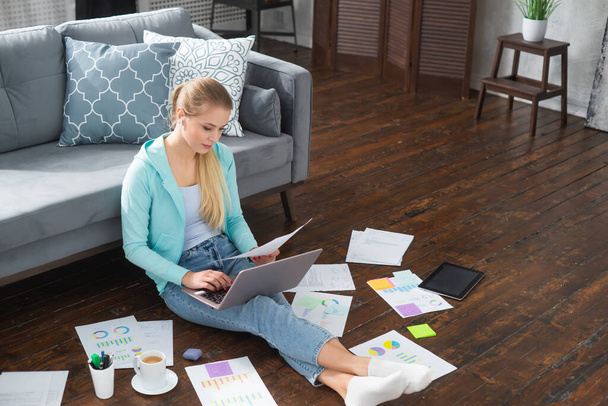 Young woman works with documents using a laptop while sitting on the floor at home. Student, entrepreneur or freelancer girl working or studying remotely via internet. - Foto, Imagen