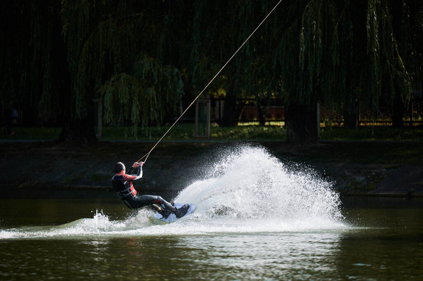 Νεαρός σέρφερ διασκεδάζει wakeboarding στο καλωδιακό πάρκο. - Φωτογραφία, εικόνα