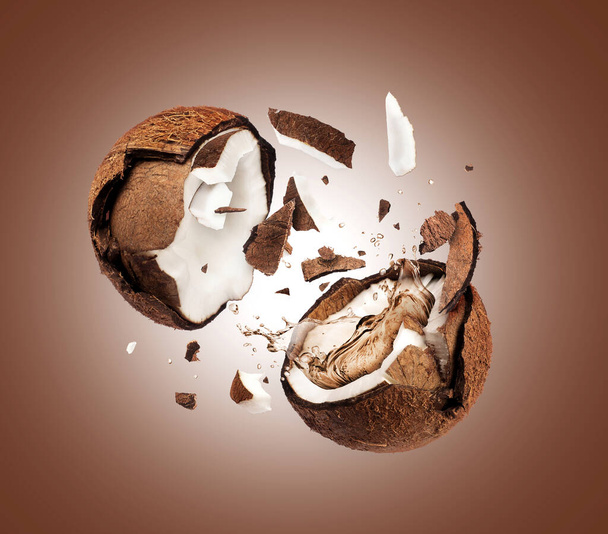 Coconut crushed in the air into two halves on brown background - Foto, immagini