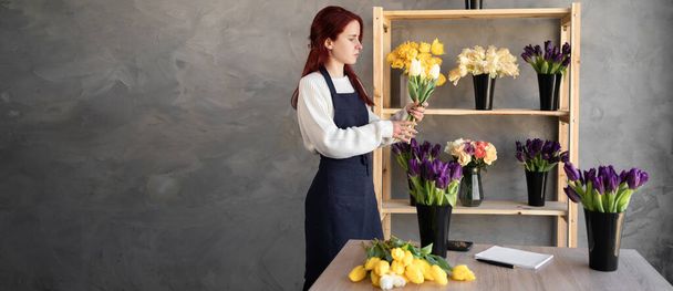 Floristin bei der Arbeit eine hübsche junge Frau in einer Schürze macht einen trendigen modernen Strauß von Tulpenblüten.Baner. Kopierraum. - Foto, Bild