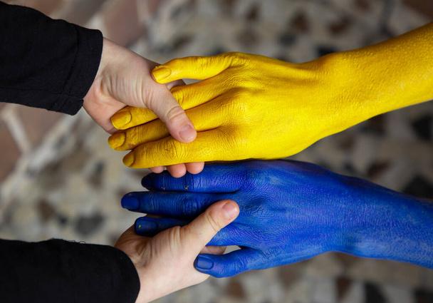 las manos de los niños sostienen las manos femeninas pintadas en color amarillo y azul de la bandera de Ucrania. Familia unida, unidad, cuidado. Apoyar a los ucranianos durante las hostilidades en el territorio de Ucrania - Foto, Imagen