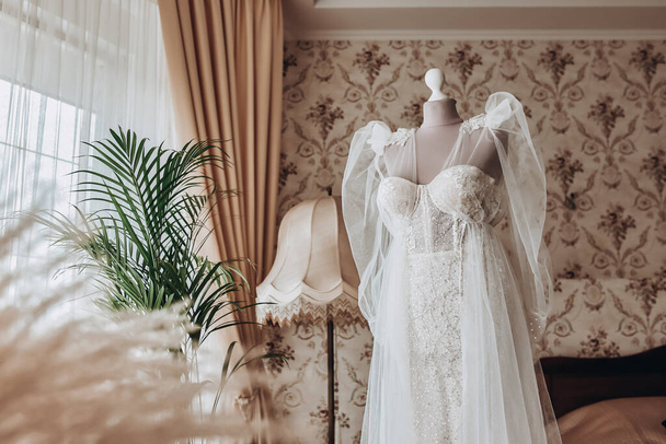 gyönyörű esküvői ruha lóg a szobában, nő készül, mielőtt szertartás - Fotó, kép