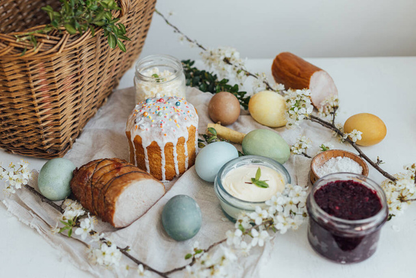 Traditional Easter basket food. Natural dyed easter eggs, stylish easter bread, ham, beets, butter, cheese on rustic wooden table with spring blossoms and linen napkin. Happy Easter! - Photo, image