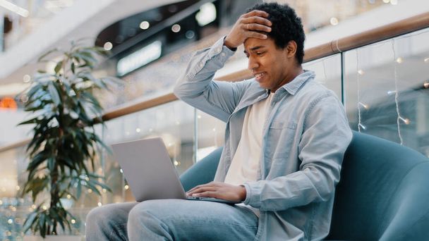 Multiracial guy freelancer african sad frustrated business man with laptop sitting on couch losing in online betting game lost money in internet auction falling stock bad news negative results failure - Photo, Image