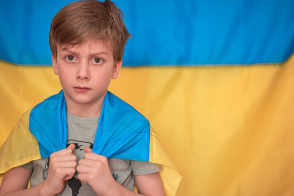 Junge mit ukrainischer gelb-blauer Fahne in der Hand. Kinder unterstützen Ukraine, indem sie Herz zeigen - Foto, Bild