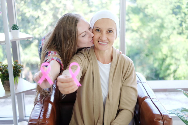 Blanke dochter kus Oudere moeder in witte hoofddoek glimlacht en houdt Bewustwording roze lint van gemeenschappelijke kanker is symbool van verschillende campagne activiteiten voor patiënten met borstkanker. - Foto, afbeelding