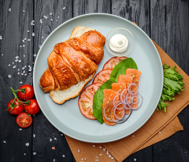 Sandwich. Croissant with salmon, cream cheese and vegetables. Serving in a cafe. Photo for the restaurant menu - Photo, Image