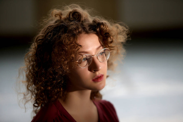 Portrait of a young girl with curly hair, with glasses - Fotó, kép