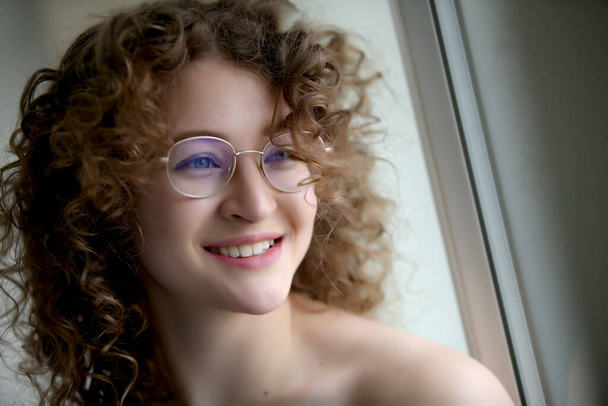 Egy göndör hajú, szemüveges fiatal lány portréja - Fotó, kép