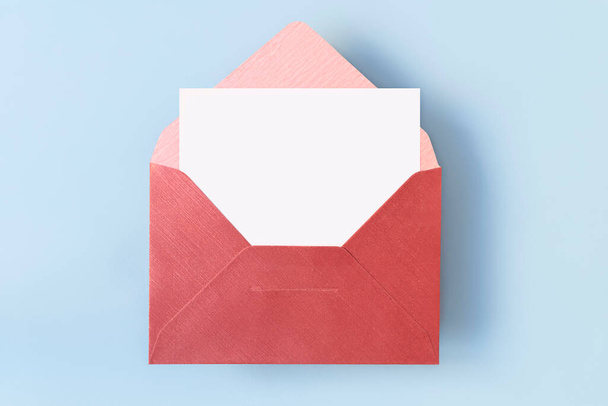 Draufsicht auf roten Umschlag mit leerer weißer Karte auf hellblauem Hintergrund - Foto, Bild