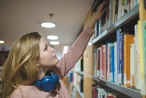 Frau wählt Bücher aus dem Bücherregal - Foto, Bild