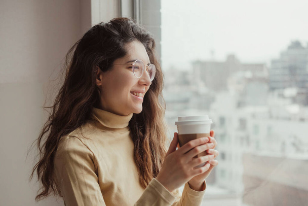 Portret van een lachende jonge vrouw die 's morgens koffie drinkt in haar hotelkamer. ontspanning concept. Reisconcept. - Foto, afbeelding
