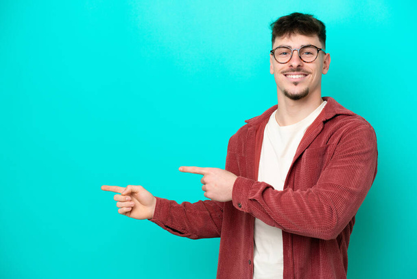 Fiatal fehér jóképű férfi elszigetelt kék háttér mutató ujját oldalra, és bemutatja a termék - Fotó, kép