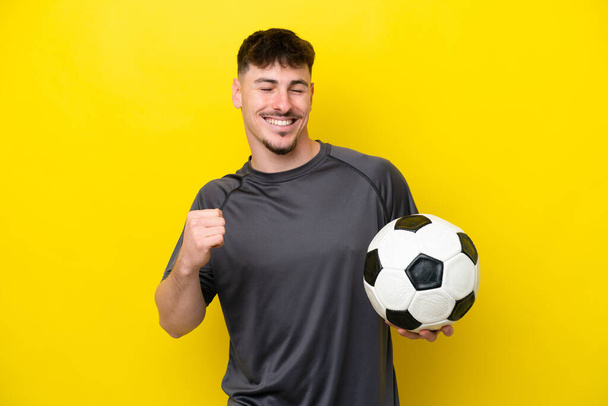 Junger Fußballer auf gelbem Hintergrund feiert einen Sieg - Foto, Bild
