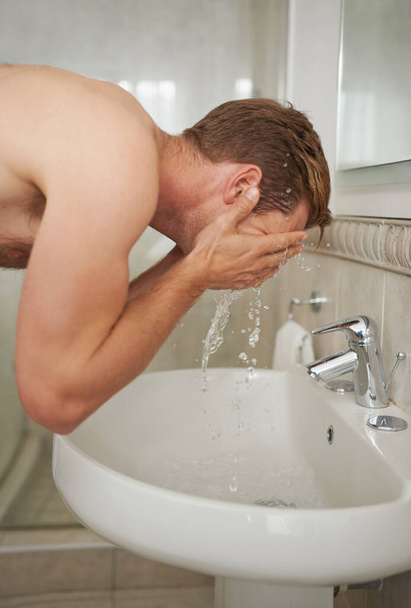 Waking up with a cold splash. A handsome man washing his face in a bathroom. - Foto, imagen