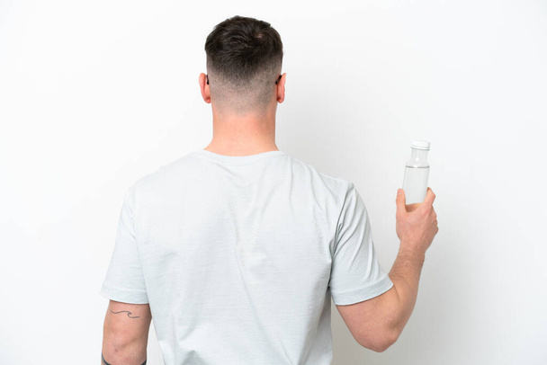 Young caucasian man holding a bottle of water isolated on white background in back position - Fotografie, Obrázek