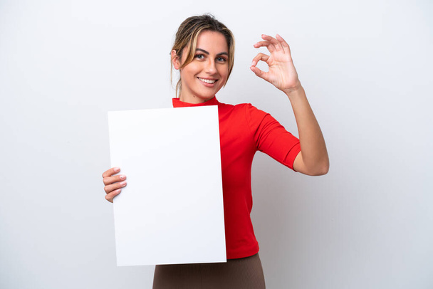 Молода біла жінка ізольована на білому тлі, тримає порожній плакат і робить знак " Гаразд"
 - Фото, зображення