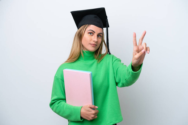 Mladá univerzita absolvent žena izolované na bílém pozadí s úsměvem a ukazující vítězství znamení - Fotografie, Obrázek