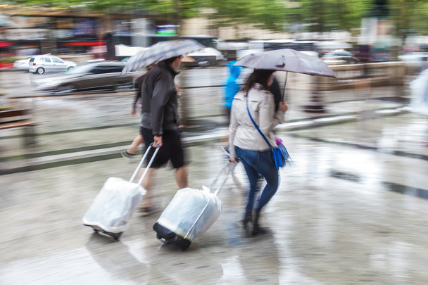 Women with trolleys and rain umbrellas walking in the rainy city - Фото, изображение