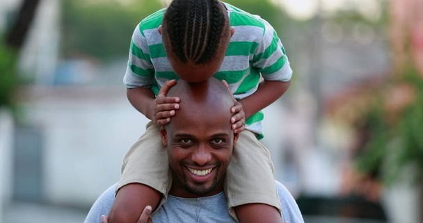 Africký otec a syn se sbližují. Kid líbání táta plešatý hlava, dítě na vrcholu otcových ramen - Fotografie, Obrázek
