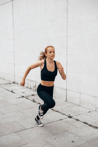 Attractive beautiful woman wearing sportswear running at urban spot. Fit woman jogging outdoor. Healthy and active lifestyle concept. - Photo, Image