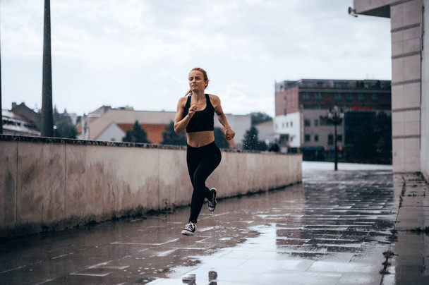 Mooi fit meisje buiten rennen in de regen. Urban run, Pijn tijdens het hardlopen - Foto, afbeelding