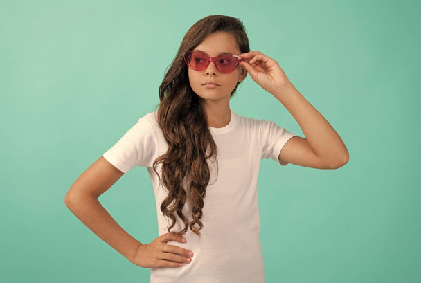 seria adolescente chica largo pelo rizado en gafas de sol estilo casual sobre fondo azul, estilo verano - Foto, Imagen