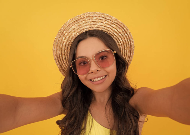 heureux enfant en été chapeau de paille et lunettes faisant selfie sur fond jaune, selfie d'été - Photo, image