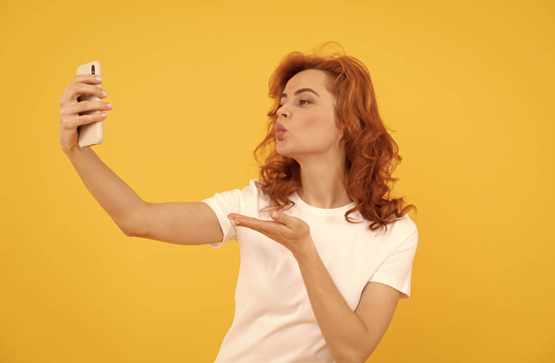 Mulher fazer mão beijando gesto para câmera telefone celular amarelo fundo, selfie - Foto, Imagem