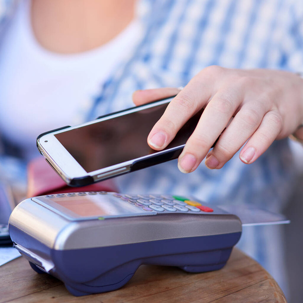 Tekniikka tekee nykyään niin helpoksi maksaa. Kuvattu tunnistamaton nainen, joka suorittaa mobiilimaksun älypuhelimellaan ja korttiautomaatilla kahvilassa. - Valokuva, kuva