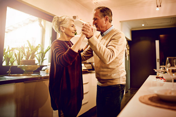 Βρίσκουν μια ξεχωριστή στιγμή κάθε μέρα. Φωτογραφία ενός ηλικιωμένου ζευγαριού να χορεύει μαζί στην κουζίνα του.. - Φωτογραφία, εικόνα