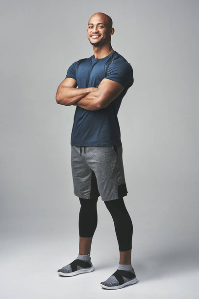 Soy adicto al fitness. Retrato de estudio de un joven atlético de pie con los brazos cruzados sobre un fondo gris. - Foto, imagen