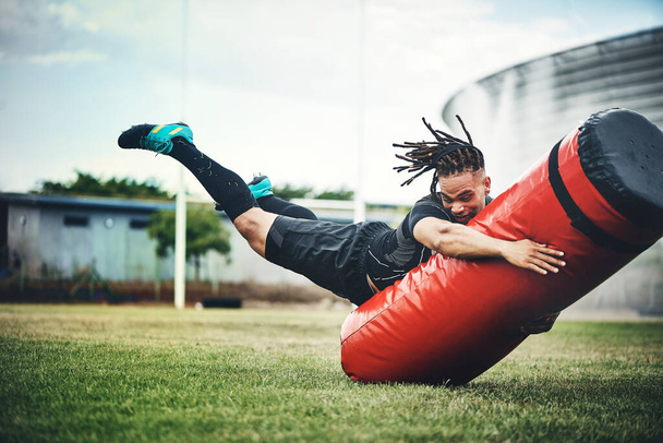 He trains like the rugby pro he is. Full length shot of a handsome young rugby player working out with a tackle bag on the playing field. - Foto, Imagem