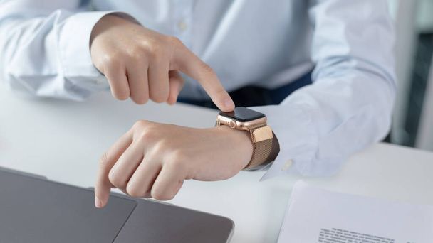 ビジネスウーマンは、腕時計に重要なメッセージをメモしたり、メモしたりするためにスマートウォッチを使用します。作業中の技術の使用,アラームアシスタント,時計時間,タッチスクリーン. - 写真・画像