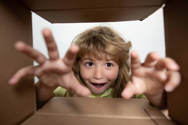 Funny excited child unpacking and opening the carton box looking inside. The little kids unboxing gift inside view. Child boy looking surprised into a gift. - Φωτογραφία, εικόνα