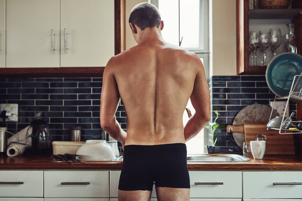 Chicoteando algo na cozinha. Foto retrovisor de um jovem musculoso de cueca enquanto prepara comida na cozinha em casa. - Foto, Imagem