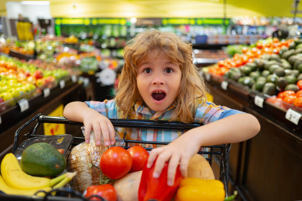 Child in the supermarket. Funny excited little boy wit shopping cart choosing goods at grocery store or supermarket. Shopping cart, grocery store concept. - Foto, Bild