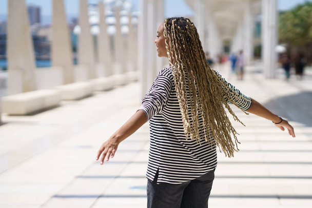 Молода чорна жінка рухає своїми кольоровими плечима на вітрі. Типова африканська зачіска. - Фото, зображення