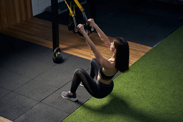 Sporty woman using hanging training straps in gym - 写真・画像