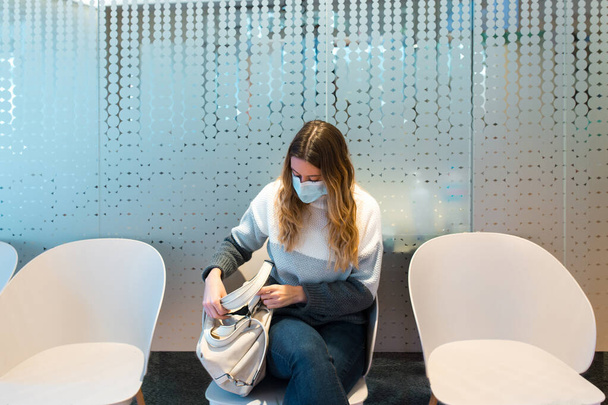 Жінка в масці для обличчя, що сидить у кімнаті очікування лікаря
. - Фото, зображення
