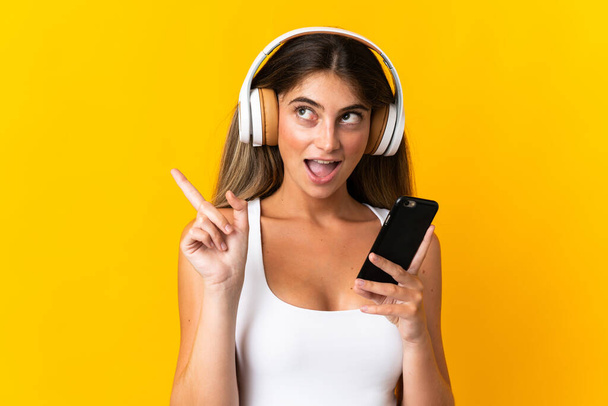 Giovane donna caucasica isolata su sfondo giallo ascoltare musica con un cellulare e cantare - Foto, immagini