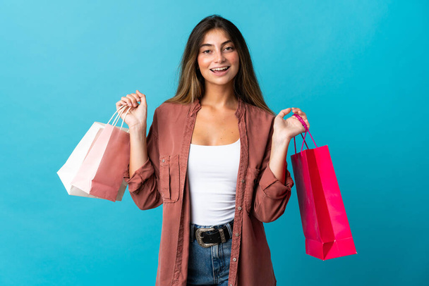 Young caucasian woman isolated on blue background holding shopping bags and smiling - Foto, Imagem