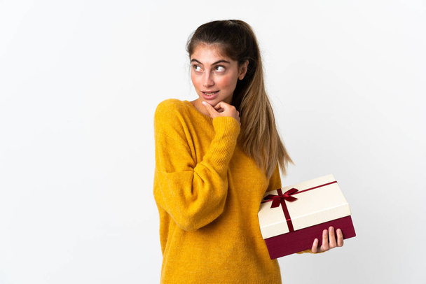 Junge Frau mit einem Geschenk auf weißem Hintergrund, das zur Seite schaut und lächelt - Foto, Bild