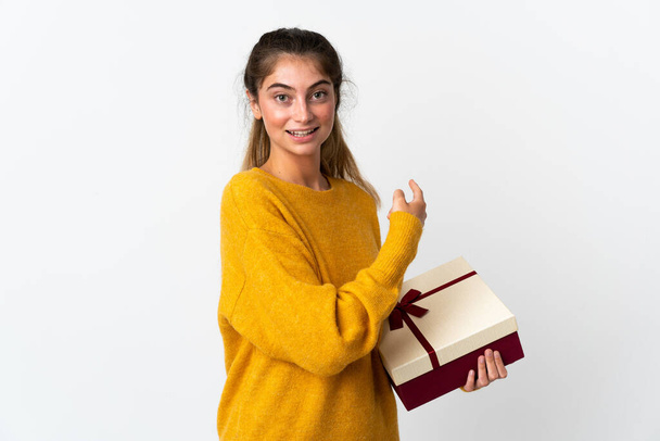 Young woman holding a gift isolated on white background pointing back - Foto, Bild
